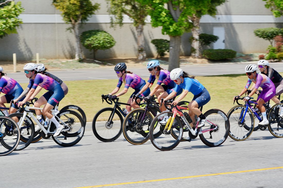 A women's road race pack riding close together on a wide road
